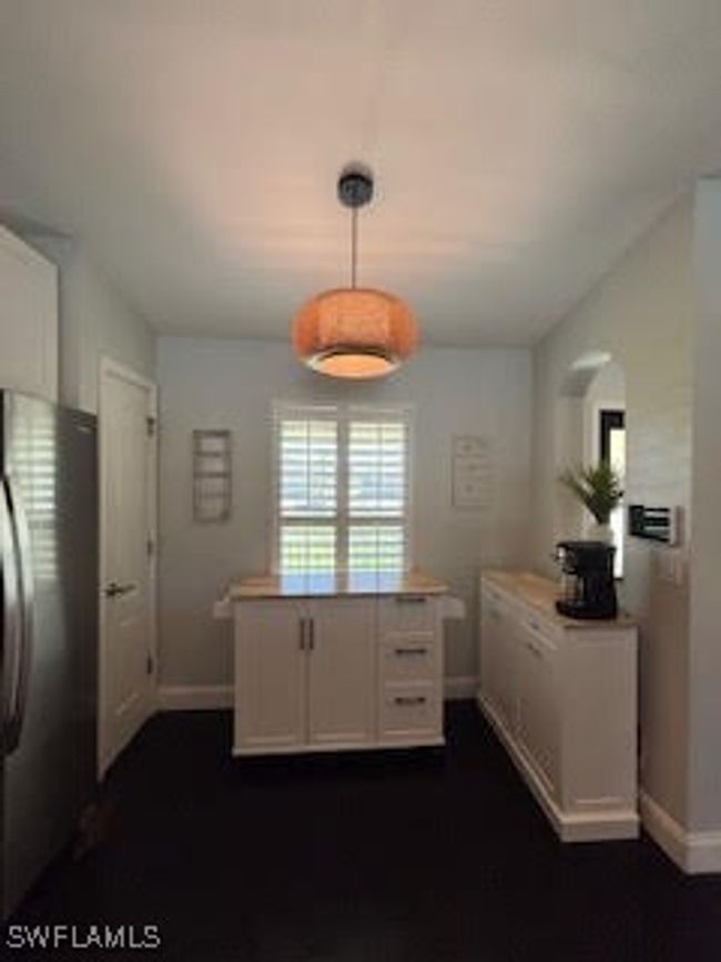 Kitchen featuring light countertops, freestanding refrigerator, hanging light fixtures, baseboards, and white cabinets | Image 6