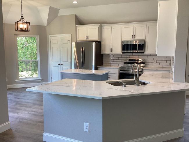 Kitchen with stainless steel appliances, a kitchen island, backsplash, light stone countertops, and vaulted ceiling | Image 8