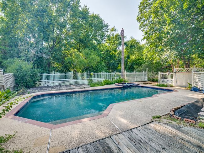 View of swimming pool with a patio, a fenced backyard, view of scattered trees, and a pool with connected hot tub | Image 15