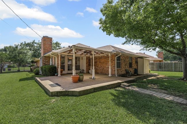 The meticulously landscaped grounds display lush greenery and well-kept gardens, highlighted by charming brick pathways and borders. Enjoy outdoor living beneath the expansive covered pergola in the backyard, ideal for entertaining or simply relaxing in a tranquil setting. | Image 20