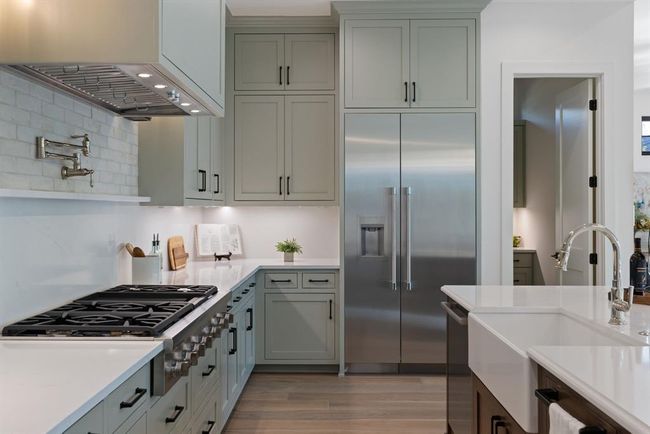 Kitchen with appliances with stainless steel finishes, wall chimney range hood, a sink, light countertops, and tasteful backsplash | Image 15