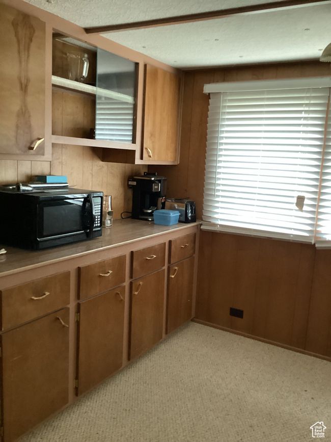 Kitchen featuring black microwave, brown cabinets, wood walls, light carpet, and light countertops | Image 6