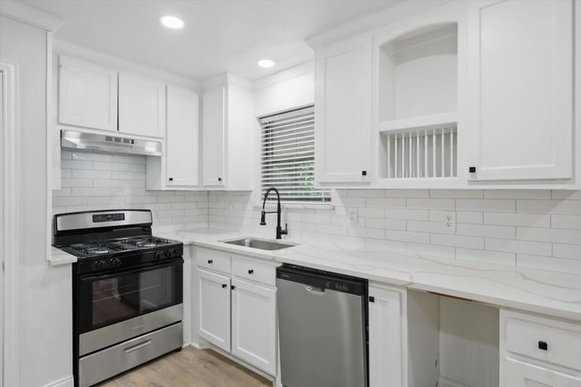 Kitchen with stainless steel appliances, a sink, under cabinet range hood, white cabinetry, and recessed lighting | Image 10