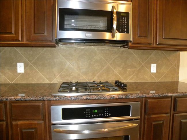 Kitchen featuring stainless steel appliances, decorative backsplash, dark stone countertops, and brown cabinets | Image 18