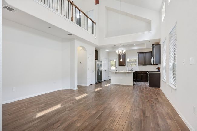 Unfurnished living room featuring arched walkways, dark wood finished floors, a towering ceiling, an inviting chandelier, and visible vents | Image 5