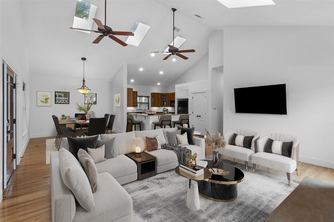 Open living area with light wood finished floors, a ceiling fan, a skylight, baseboards, and high vaulted ceiling | Image 7