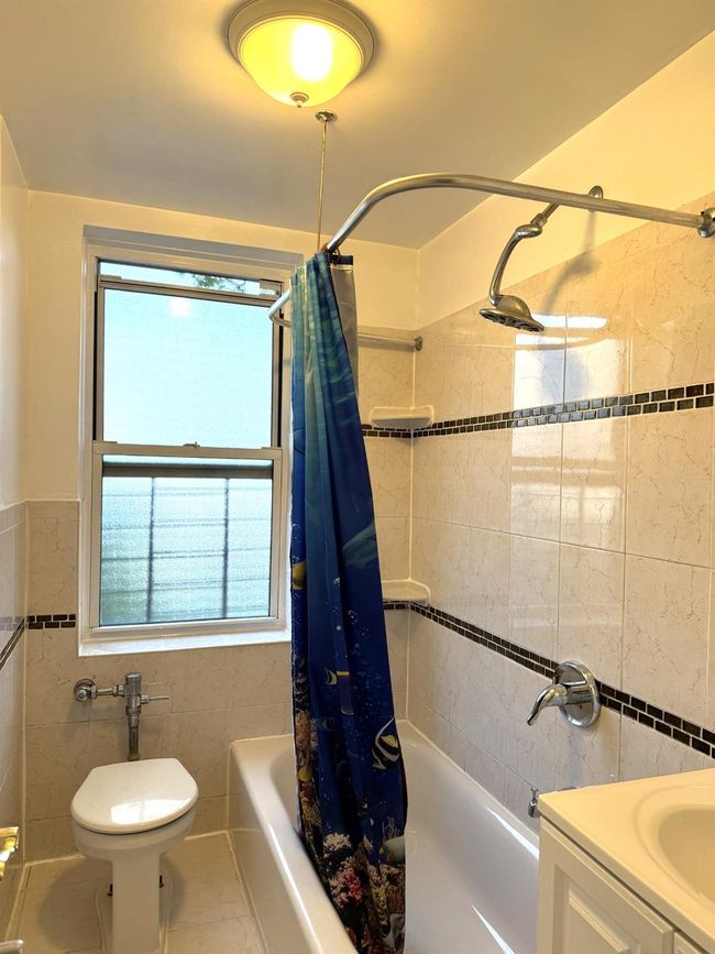 Bathroom featuring tile walls, shower / bath combination with curtain, healthy amount of natural light, vanity, and wainscoting | Image 19