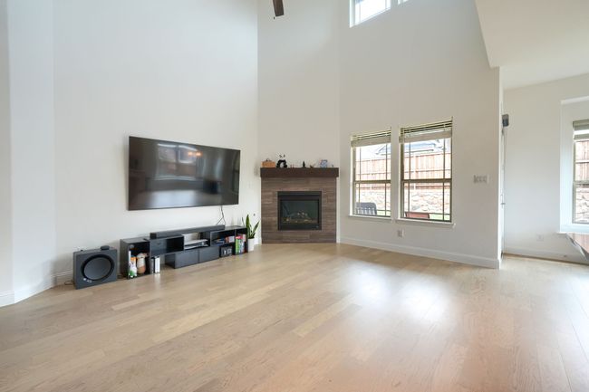 Living room featuring a fireplace, wood finished floors, a towering ceiling, and baseboards | Image 9