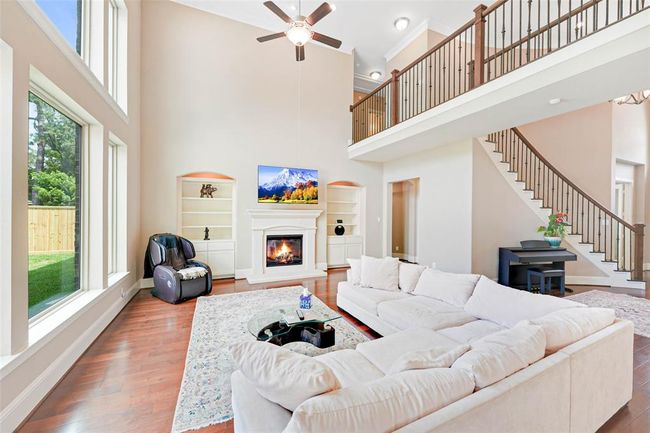 Grand living room with soaring ceilings, dramatic wall of windows, and a cozy fireplace framed by built-in shelving.he open railing upstairs and curved staircase add architectural charm and a bright, open feel. | Image 19