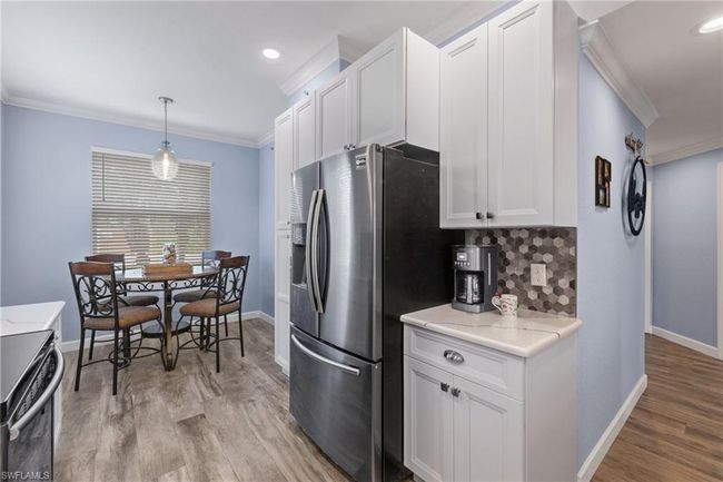 Kitchen featuring stainless steel fridge with ice dispenser, range with electric stovetop, ornamental molding, pendant lighting, and white cabinets | Image 6