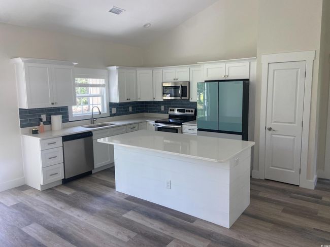 Kitchen with appliances with stainless steel finishes, tasteful backsplash, white cabinets, a kitchen island, and high vaulted ceiling | Image 12