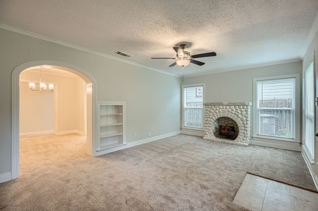 Unfurnished living room featuring visible vents, a textured ceiling, carpet, arched walkways, and ceiling fan with notable chandelier | Image 6
