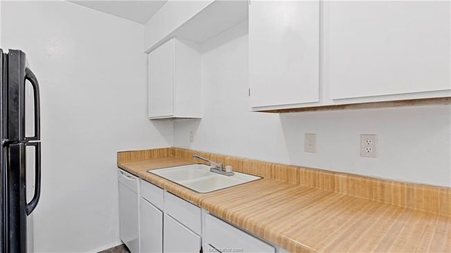 Kitchen featuring black fridge, white cabinetry, white dishwasher, and sink | Image 22