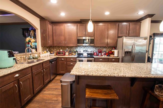 Kitchen featuring appliances with stainless steel finishes, a sink, crown molding, a kitchen bar, and backsplash | Image 12