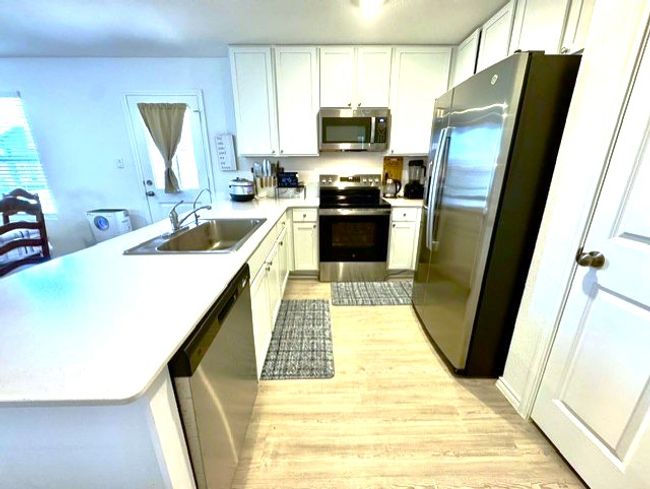 Kitchen featuring appliances with stainless steel finishes, a peninsula, light wood-type flooring, and light countertops | Image 6