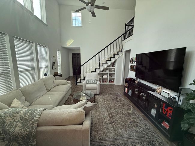 Living area with ceiling fan, stairway, wood finished floors, and a high ceiling | Image 5