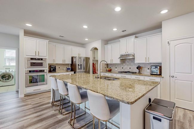 Kitchen with a sink, appliances with stainless steel finishes, washer / clothes dryer, under cabinet range hood, and light wood-style flooring | Image 16
