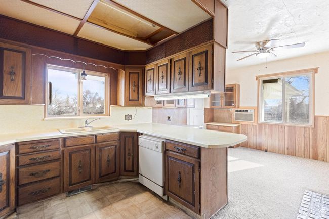 Kitchen featuring light countertops, a sink, a ceiling fan, wainscoting, and white dishwasher | Image 25