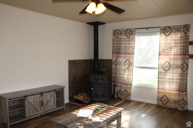 Living room with a wood stove, dark wood-style flooring, ceiling fan, and baseboards | Image 4