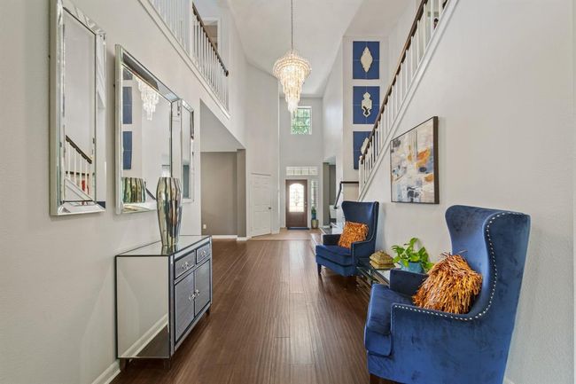 The spacious foyer boasts an open feel with high ceilings, crisp neutral tones, and beautiful architectural details, including a stunning light fixture and upper-level balcony view. | Image 7