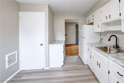 Kitchen featuring white fridge, sink, light wood-type flooring, and white cabinetry | Image 3