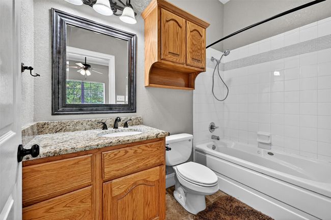 Bathroom with bathtub / shower combination, vanity, toilet, tile patterned floors, and a textured wall | Image 31