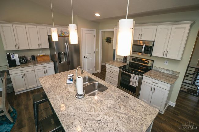 Granite counters accent the soft white cabinets. Brushed nickel light fixtures and plumbing fixtures. Vaulted ceiling continues into the Great Room space. | Image 9
