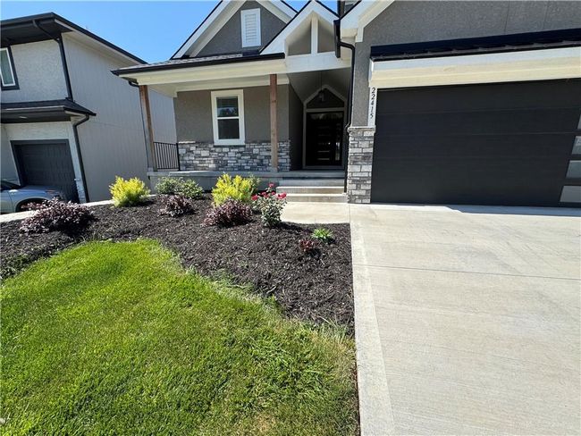 View of front of property with driveway, stone siding, a porch, a garage, and stucco siding | Image 65