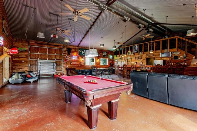 Rec room with a ceiling fan, wood walls, concrete flooring, billiards, and high vaulted ceiling | Image 6