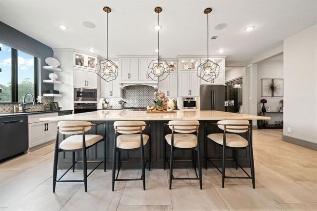 This modern kitchen features a spacious island with seating, stylish pendant lighting, and sleek cabinetry. Large windows provide natural light, while stainless steel appliances and a decorative backsplash add a touch of elegance. Perfect for cooking and entertaining. | Image 16