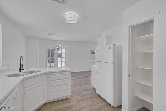 Kitchen featuring white appliances, a peninsula, a chandelier, white cabinets, and light countertops | Image 10
