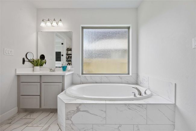 This bathroom features a modern, elegant design with a spacious marble-tiled bathtub, a large frosted window for natural light, and a sleek vanity area with ample storage and contemporary fixtures. | Image 25