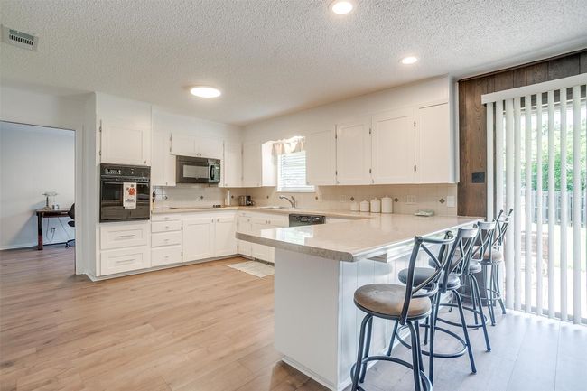 Kitchen with black appliances, a peninsula, white cabinets, backsplash, and a textured ceiling | Image 16