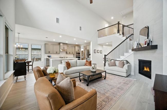 Living room featuring a towering ceiling, light wood-style floors, a fireplace, recessed lighting, and stairs | Image 9