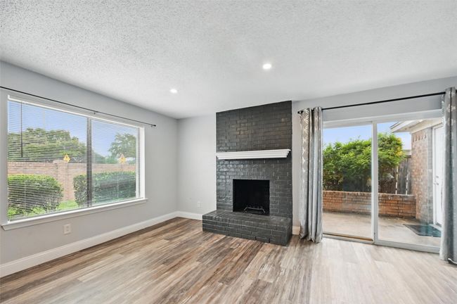 Unfurnished living room with wood finished floors, plenty of natural light, recessed lighting, a brick fireplace, and a textured ceiling | Image 4