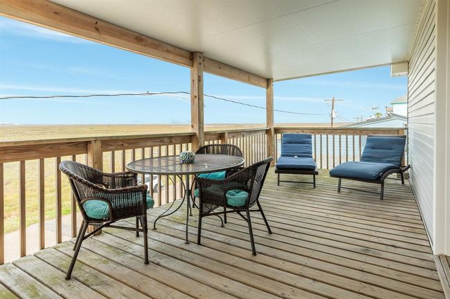 This photo shows the spacious, covered wooden back deck with a seating area, including a round table and cushioned chairs. It offers expansive views of open bay views, perfect for relaxation and outdoor enjoyment. | Image 20