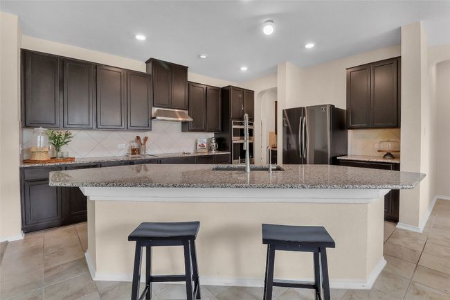 Kitchen featuring appliances with stainless steel finishes, under cabinet range hood, arched walkways, a kitchen breakfast bar, and recessed lighting | Image 8