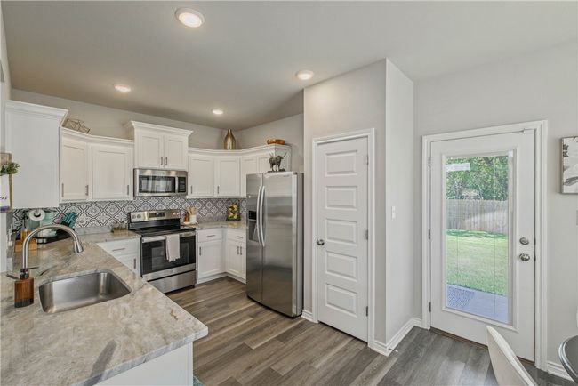 Kitchen featuring stainless steel appliances, backsplash, light stone counters, white cabinets, and dark wood-type flooring | Image 10