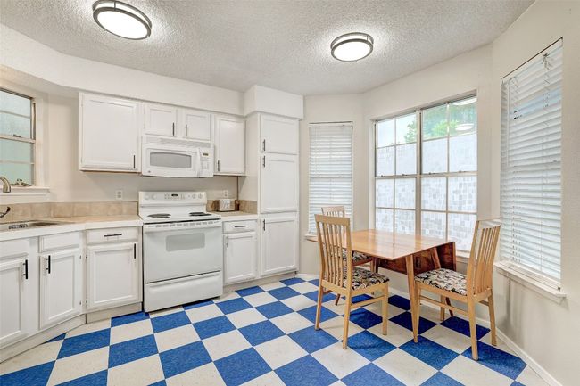 Kitchen with white appliances, light floors, a textured ceiling, a sink, and white cabinetry | Image 7