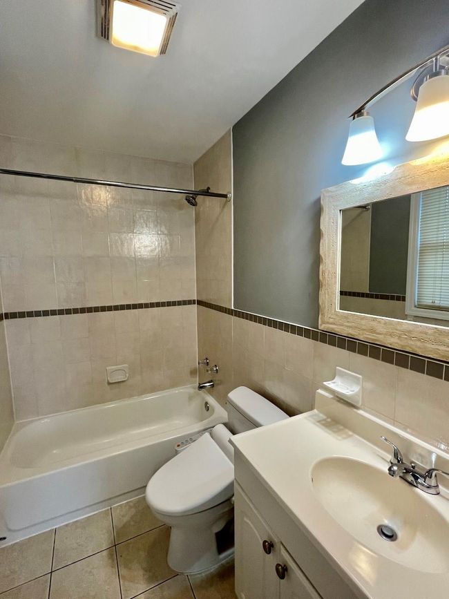 Full bathroom featuring toilet, tile walls, bathtub / shower combination, vanity, and tile patterned floors | Image 13