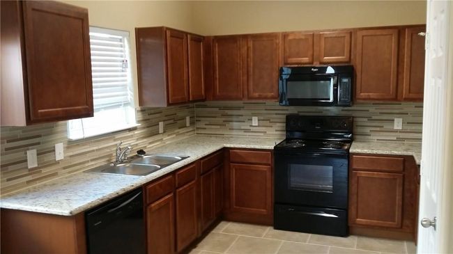 Kitchen featuring black appliances, backsplash, brown cabinetry, and light tile patterned flooring | Image 4