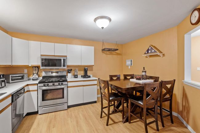 Kitchen with light wood finished floors, white cabinets, a toaster, light countertops, and appliances with stainless steel finishes | Image 4