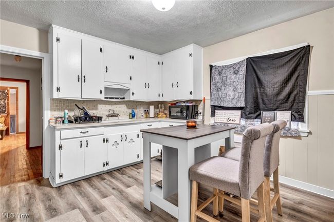 Kitchen with decorative backsplash, light wood-style floors, a textured ceiling, and white cabinets | Image 4