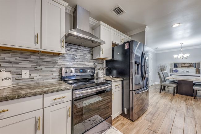 Kitchen with stainless steel appliances, wall chimney exhaust hood, crown molding, a chandelier, and white cabinets | Image 13
