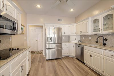 Kitchen featuring white cabinets, stainless steel appliances, light hardwood / wood-style flooring, ceiling fan, and sink | Image 3