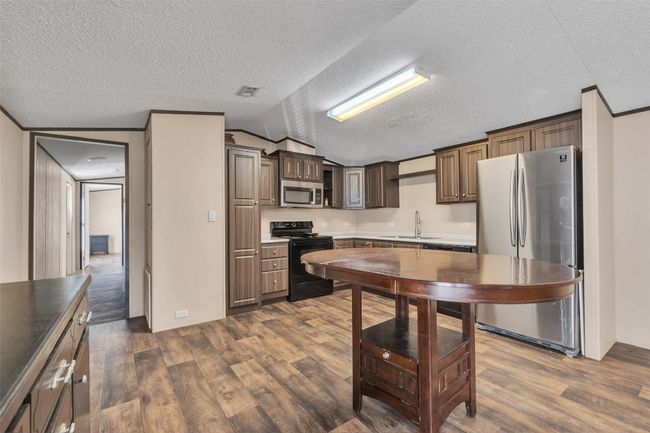 Kitchen featuring appliances with stainless steel finishes, dark wood-style floors, lofted ceiling, a textured ceiling, and light countertops | Image 6