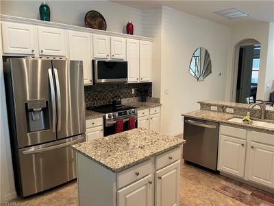 Kitchen featuring sink, tasteful backsplash, a kitchen island, white cabinetry, and stainless steel appliances | Image 3