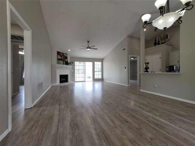 Unfurnished living room featuring a ceiling fan, baseboards, a fireplace, wood finished floors, and high vaulted ceiling | Image 6