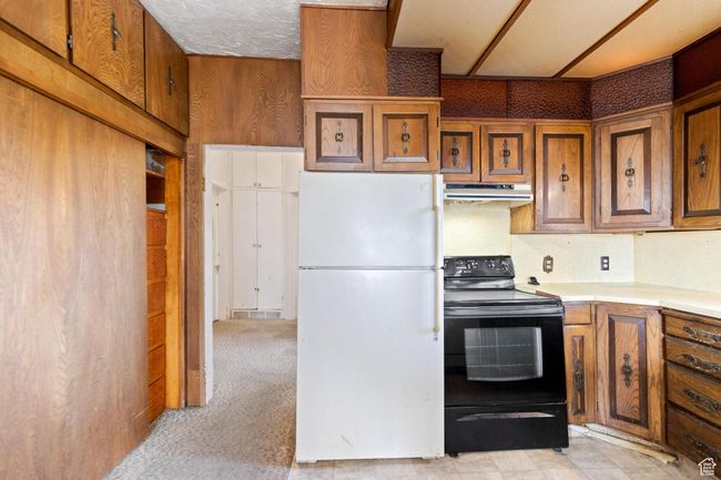 Kitchen featuring light countertops, freestanding refrigerator, brown cabinetry, under cabinet range hood, and black / electric stove | Image 24