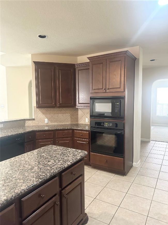 Kitchen featuring black appliances, arched walkways, light tile patterned floors, dark brown cabinetry, and dark stone​​‌​​​​‌​​‌‌​‌‌​​​‌‌​​‌‌​‌​​​​​‌ countertops | Image 4